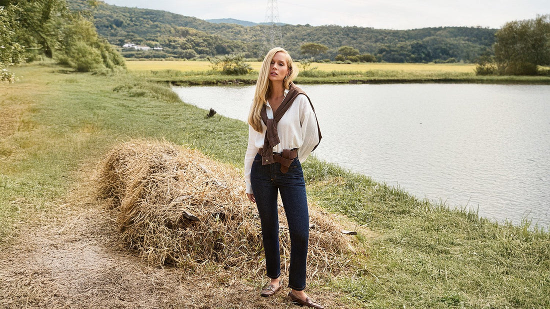 Modelo usando calça jeans e camisa branca em uma area rural com lago no fundo