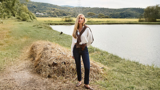 Modelo usando calça jeans e camisa branca em uma area rural com lago no fundo
